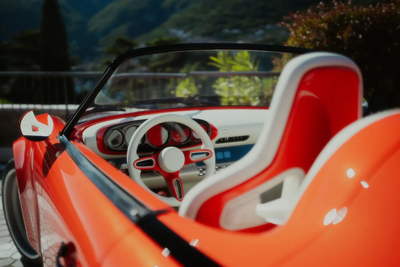 The cream-rimmed steering wheel and a vermilion Recaro seat, Lake Como beyond the windscreen